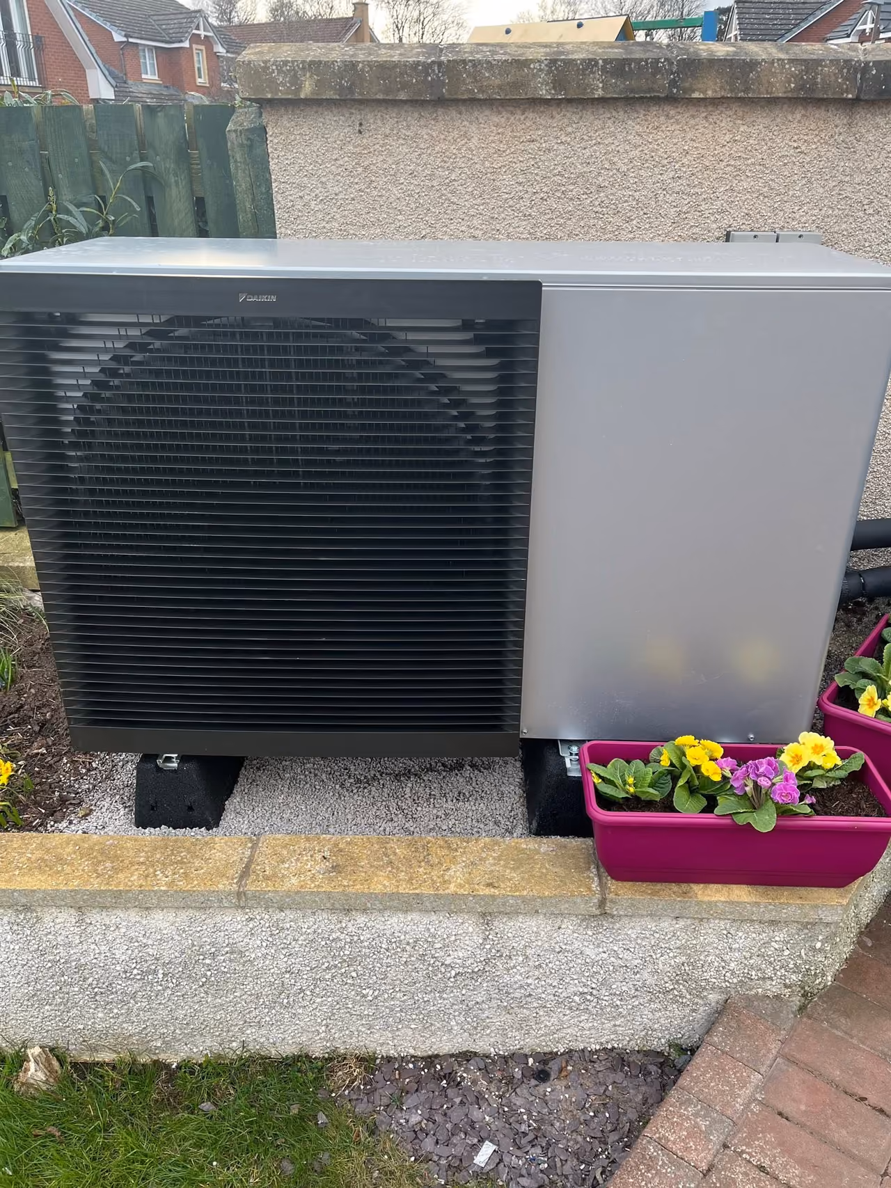 Daikin air source heat pump installed beside a garden and flower planters